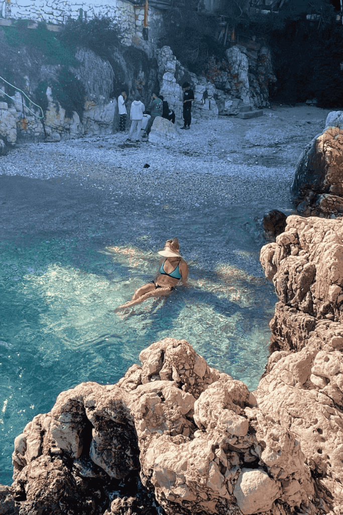 Kate floats peacefully in the crystal-clear shallows of Small Pebble Beach in Kaş, Turkey, surrounded by smooth rocks and tranquil turquoise water.