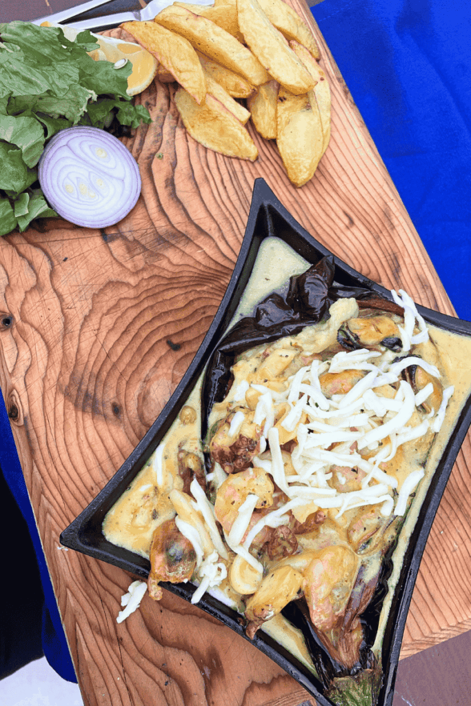 Baked eggplant dish with shrimp, melted cheese, and potato wedges on a rustic wooden board.