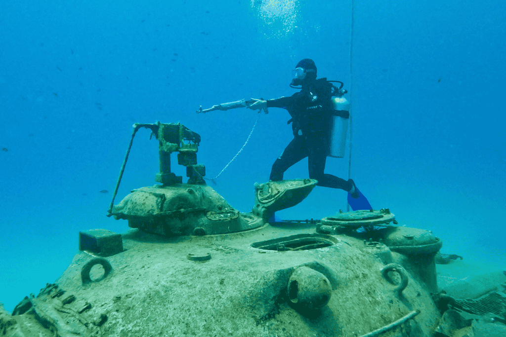 Kate playfully aims a faux weapon while floating beside the turret of a submerged tank in crystal-clear waters off the coast of Kaş.