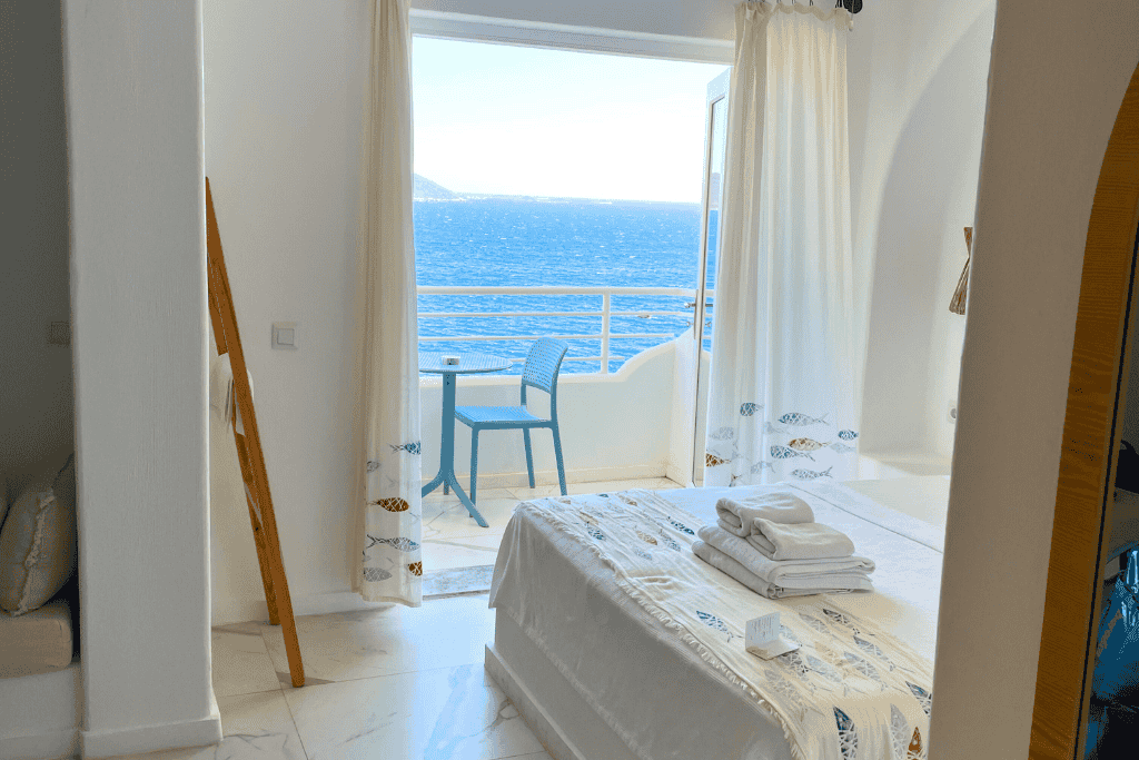 Bright, whitewashed hotel room in Kaş with ocean-themed decor and a balcony overlooking the deep blue sea.