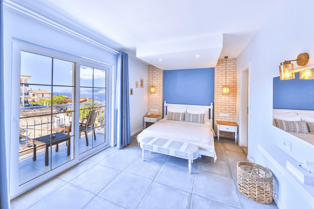 Bright and airy hotel room in Kaş with coastal blue accents, a private balcony, and views of the sea and nearby rooftops.