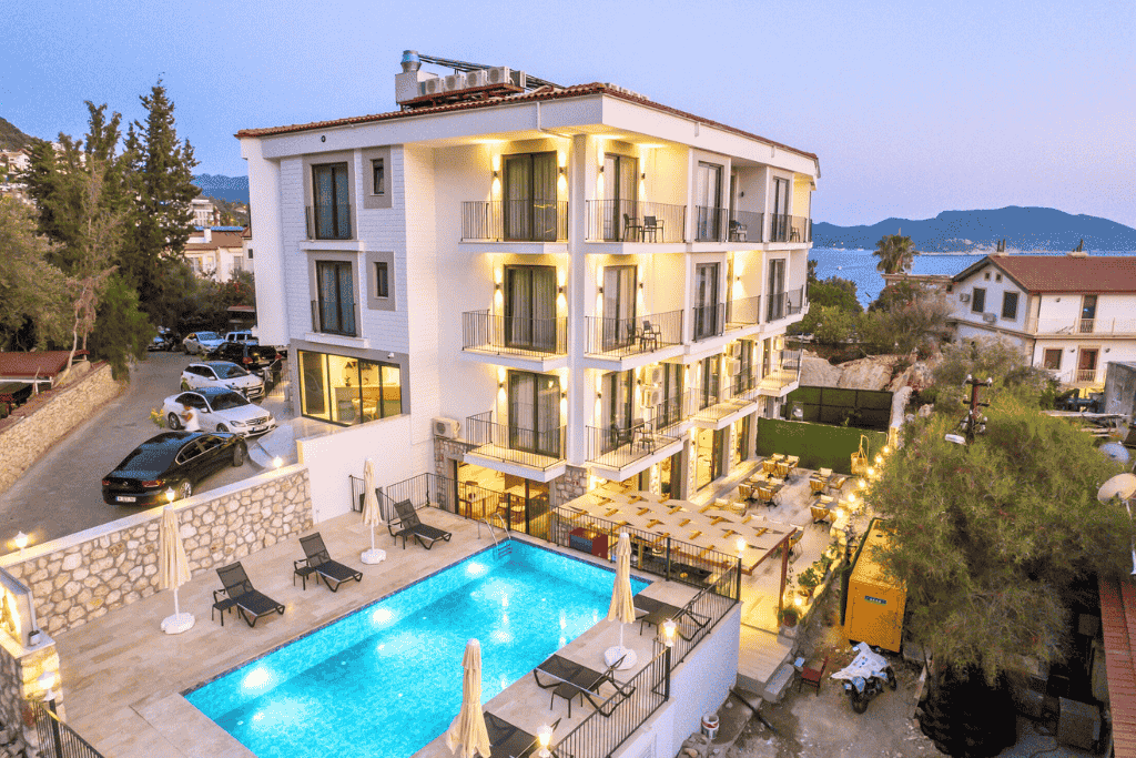 Modern boutique hotel in Kaş with balconies, a glowing pool area, and partial sea views at twilight.