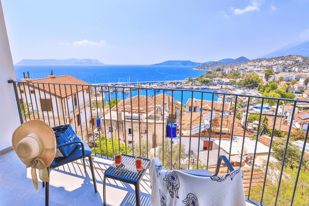 Balcony view from a hotel in Kaş overlooking terracotta rooftops, the marina, and the sparkling blue Mediterranean Sea.