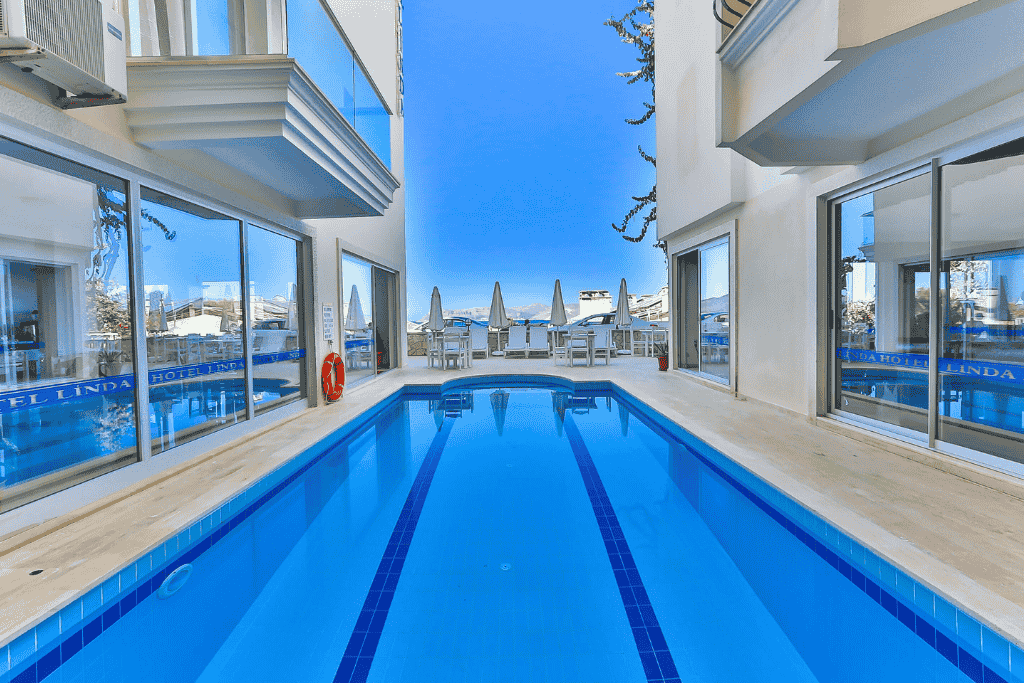 Narrow hotel pool in Kaş nestled between two buildings, with a glimpse of the sea and outdoor seating beyond.
