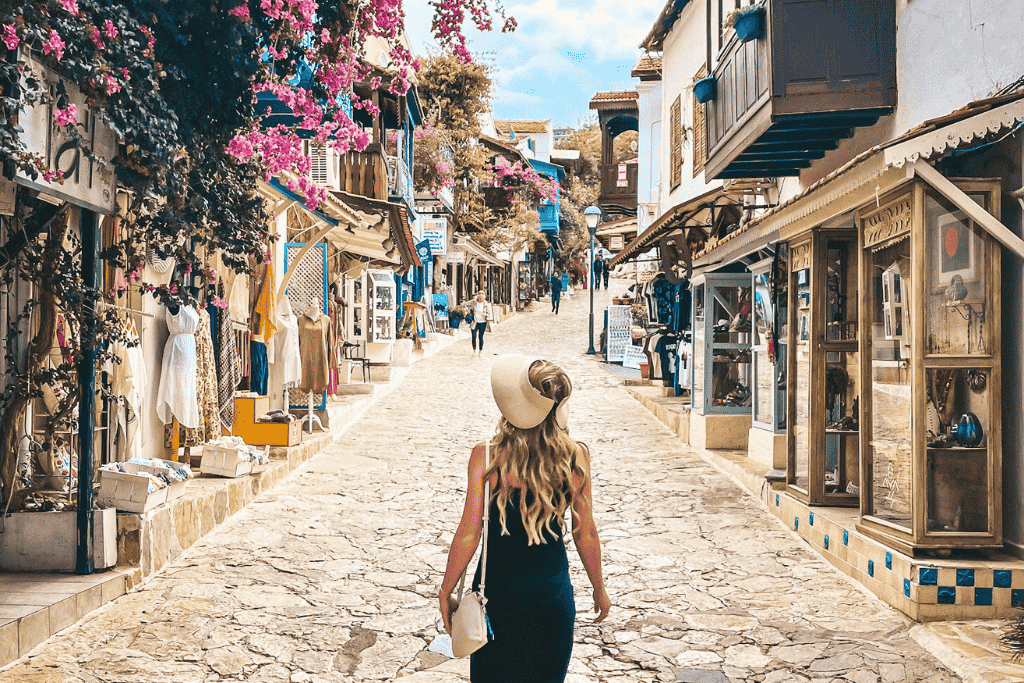 Kate in a sunhat walks up a charming cobblestone street in Kaş lined with boutiques, flowers, and traditional architecture.