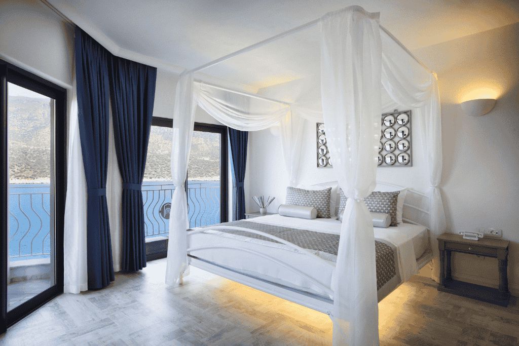 Elegant hotel room in Kaş with a canopy bed, modern decor, and floor-to-ceiling windows overlooking the sea.