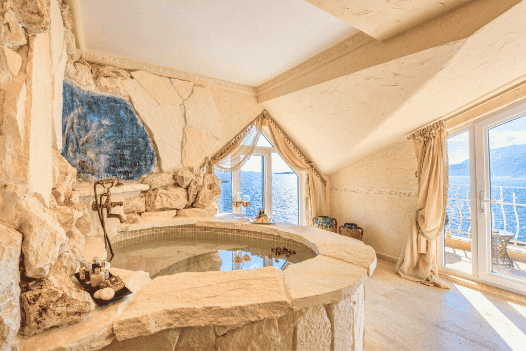 Rustic-style stone jacuzzi room in a Kaş hotel, with arched windows framing serene sea and mountain views.