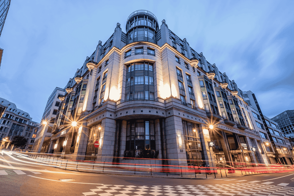 Striking corner view of the Radisson Collection Grand Place Brussels, with its grand façade lit up at dusk and light trails from passing traffic adding motion to the elegant scene.