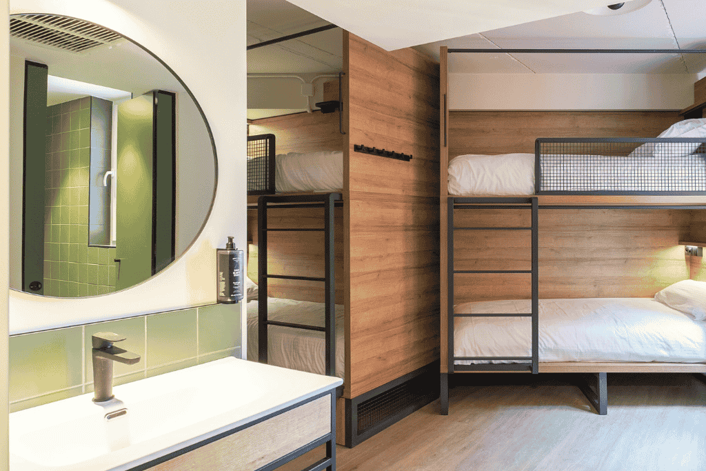 Modern, minimalist room at Latroupe Grand Place in Brussels featuring wooden bunk beds, a sleek green-tiled bathroom, and contemporary industrial accents.

