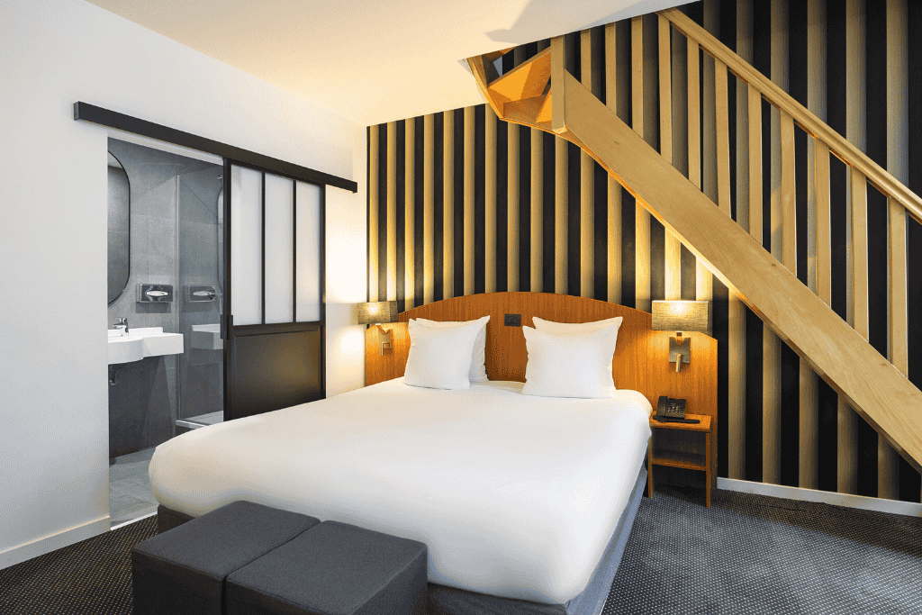 Stylish hotel room at Hotel Aris Grand Place featuring a modern black-and-gold striped accent wall, a cozy double bed, and an open-plan bathroom with sleek finishes.

