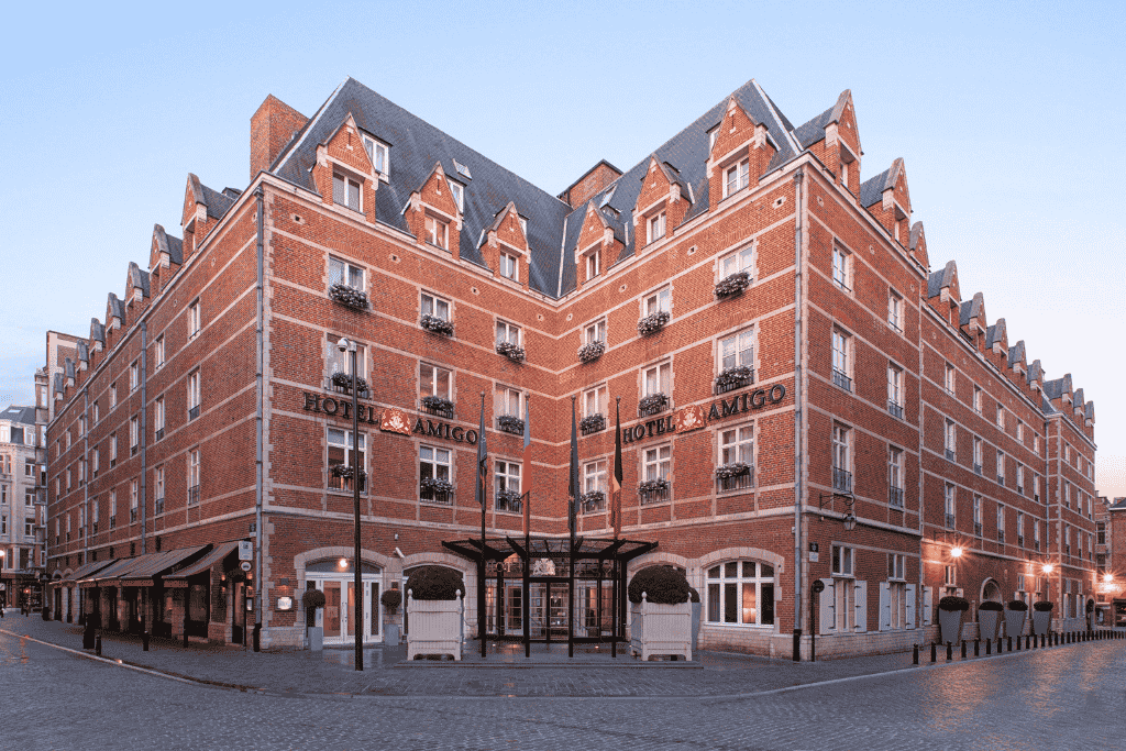 Elegant red-brick exterior of Rocco Forte Hotel Amigo in Brussels, showcasing its classic architecture with flower-box balconies and a grand corner entrance near the Grand Place.