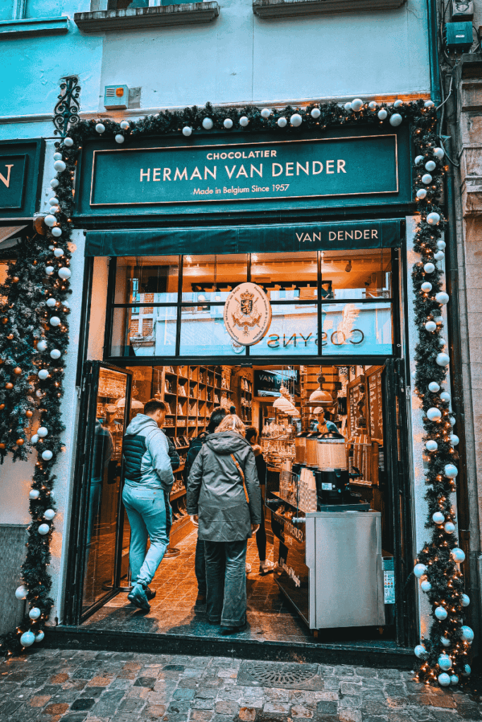 The festive storefront of Herman Van Dender chocolatier in Brussels is adorned with Christmas garlands and ornaments as customers browse the elegant interior filled with Belgian chocolate.
