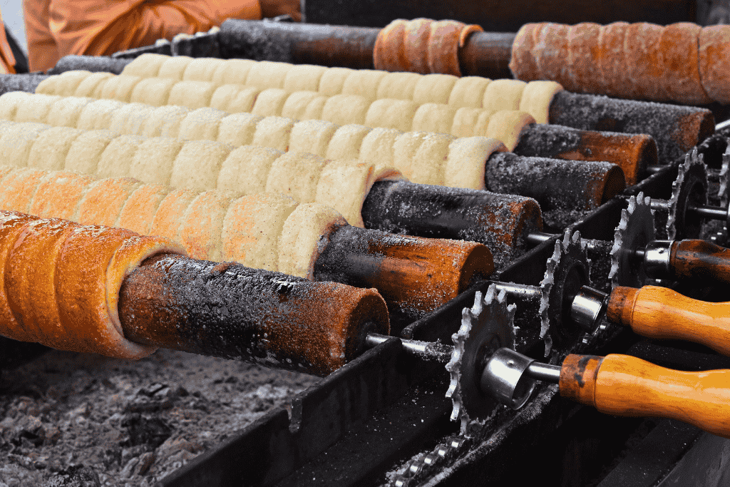 Rows of chimney cakes, or kürtőskalács, are slowly roasted on wooden rollers over open coals, with some already golden brown and others still baking.