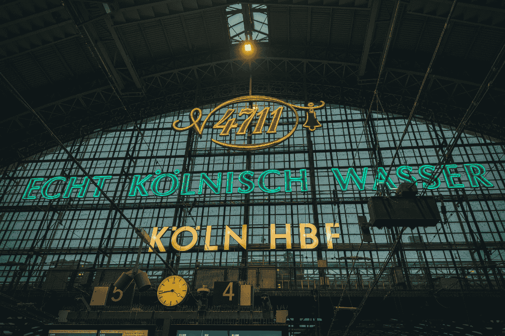 Illuminated signage reading “4711 Echt Kölnisch Wasser Köln HBF” glows inside Cologne’s central train station beneath its massive arched glass roof.