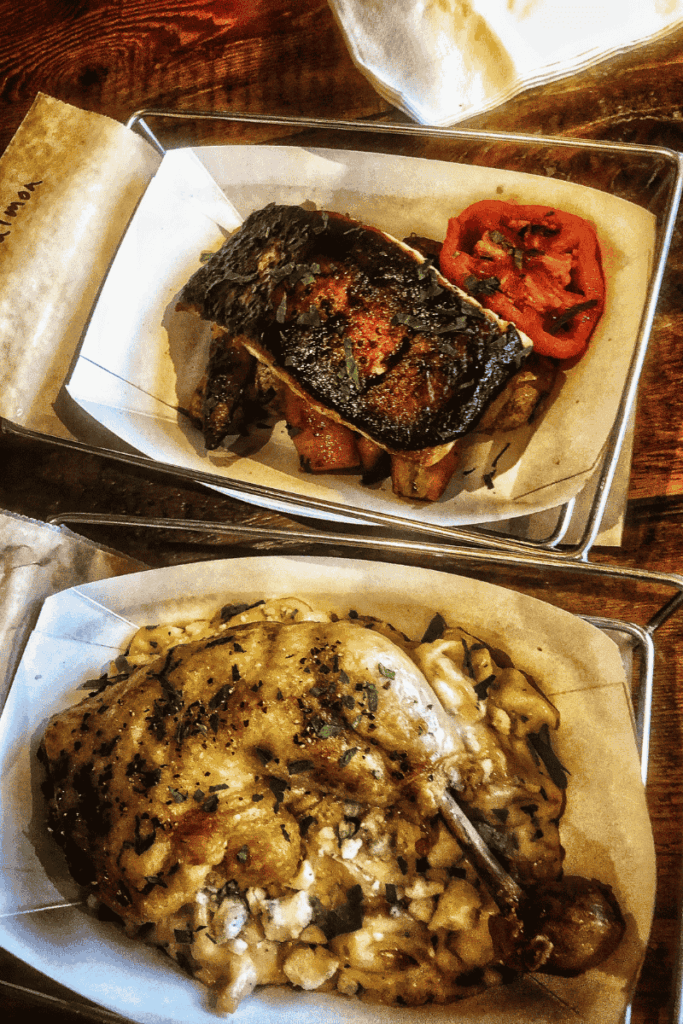 A farm-to-table meal is served with roasted chicken over creamy gnocchi and a charred vegetable-topped entrée with tomatoes, all plated on parchment-lined trays.