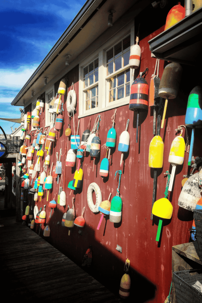 A red wooden building in Bar Harbor, Maine is decorated with dozens of brightly colored fishing buoys and a few life rings hanging along its side.