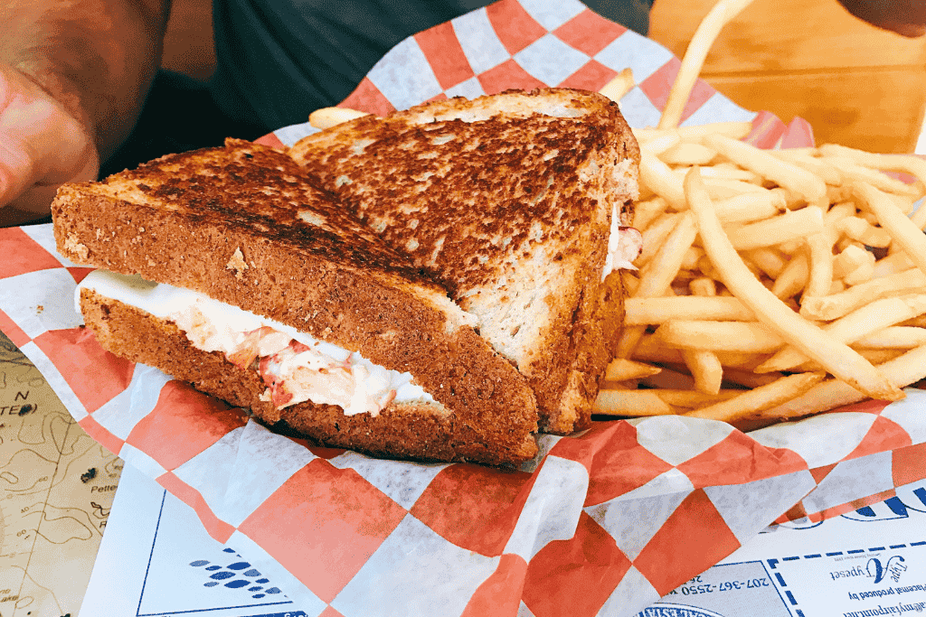 A lobster patty melt packed with rich filling is grilled to perfection and paired with a heap of crispy fries on red-and-white checkered paper.