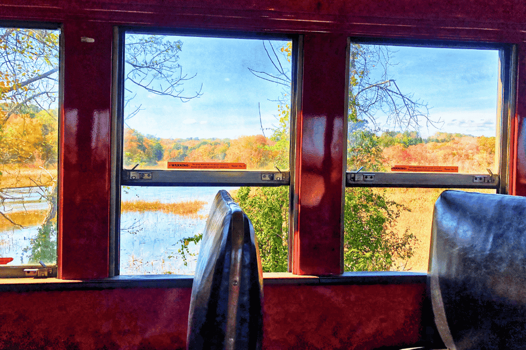 A scenic view of marshland and vibrant autumn trees is seen through the windows of the Essex steam train in Connecticut.