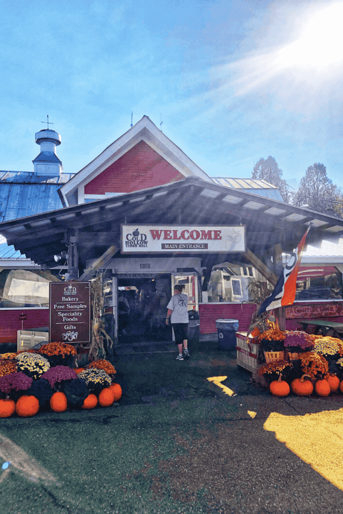 The entrance to Cold Hollow Cider Mill in Vermont is decorated with bright mums and pumpkins, welcoming visitors with signs for free samples and specialty foods.