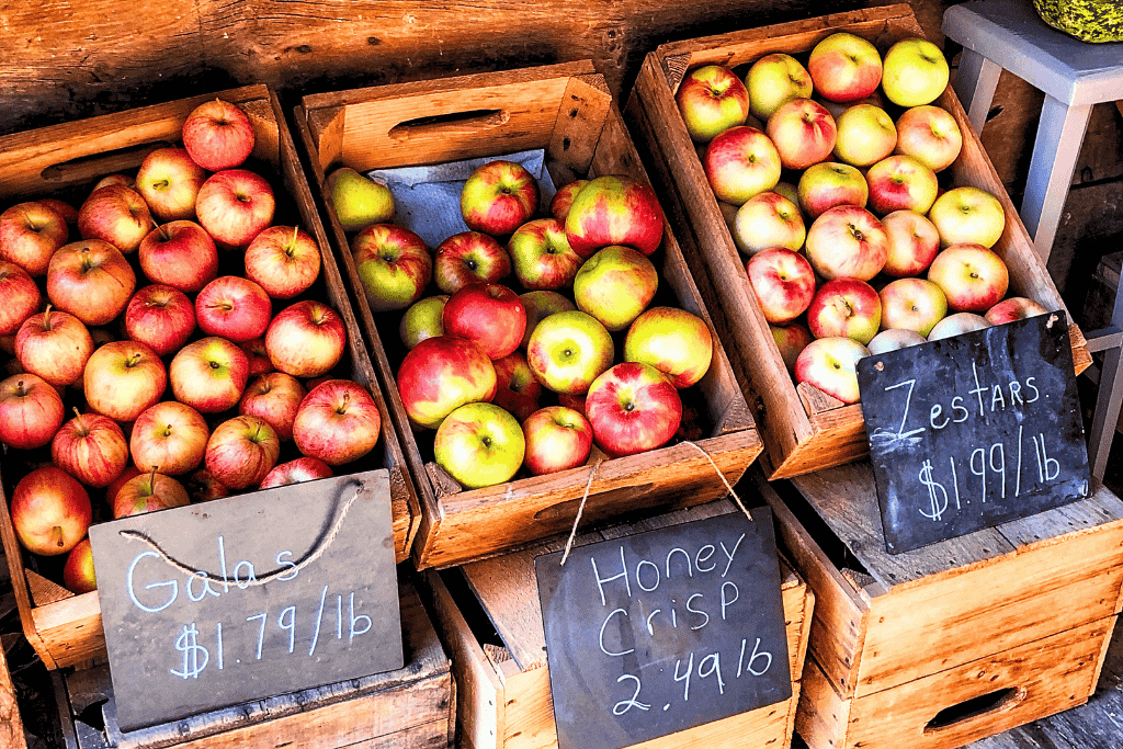 Wooden crates display fresh Vermont apples—Galas, Honey Crisp, and Zestars—each labeled with handwritten pricing on chalkboard signs.