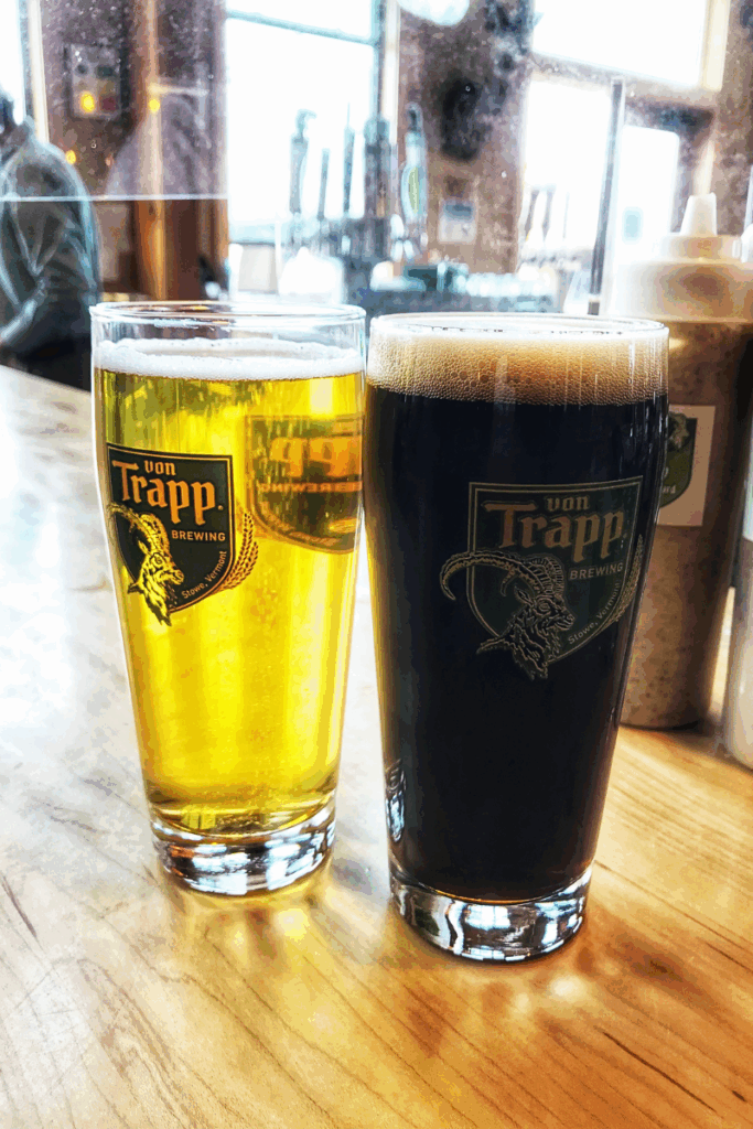 Two pints of beer from von Trapp Brewing, one light and one dark, sit on a wooden bar with taps in the background.
