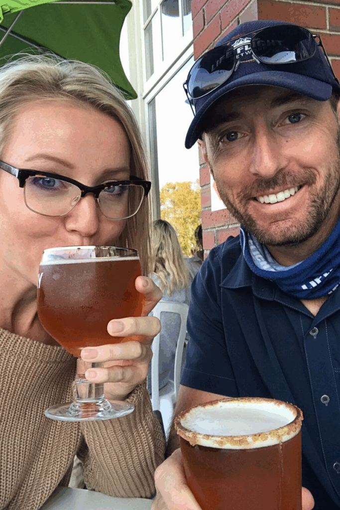 Kate and her husband enjoy drinks on an outdoor patio, smiling with their beers in hand on a sunny day.