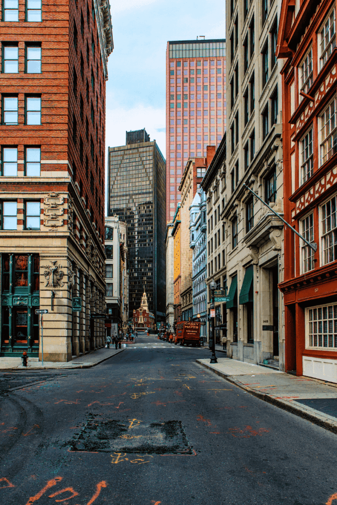 Street view in downtown Boston lined with historic and modern buildings, leading toward the Old State House at the end of the block.