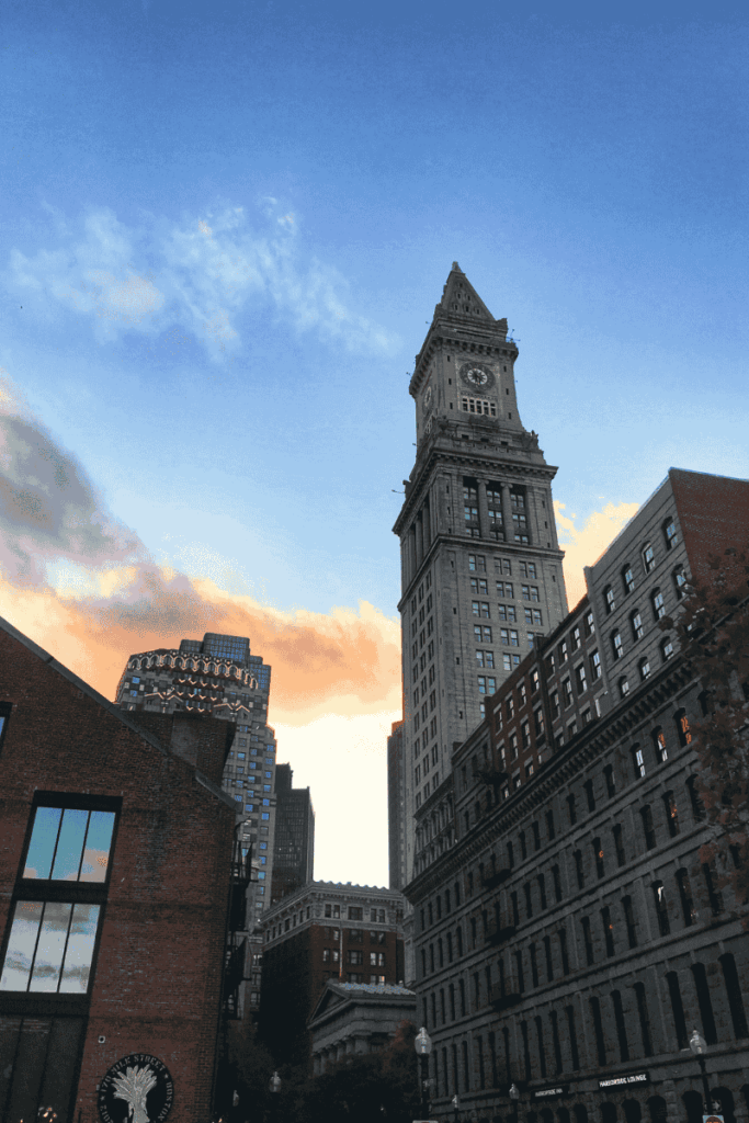 The Custom House Tower in Boston framed by surrounding buildings and a colorful sunset sky. A dramatic architectural moment.