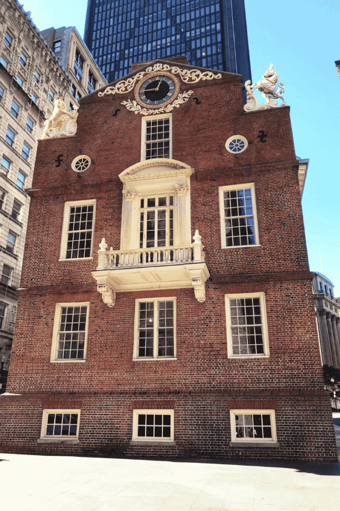 Front view of the Old State House in Boston with its red brick facade, white balcony, and ornamental clock, framed by modern skyscrapers. A must-see Revolutionary landmark during a weekend getaway in Boston.