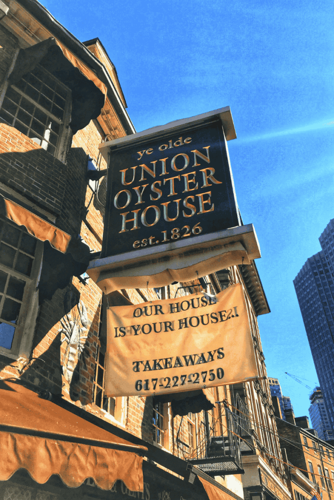 Historic signage for Ye Olde Union Oyster House, established in 1826, hanging above a brick building under a bright blue sky.
