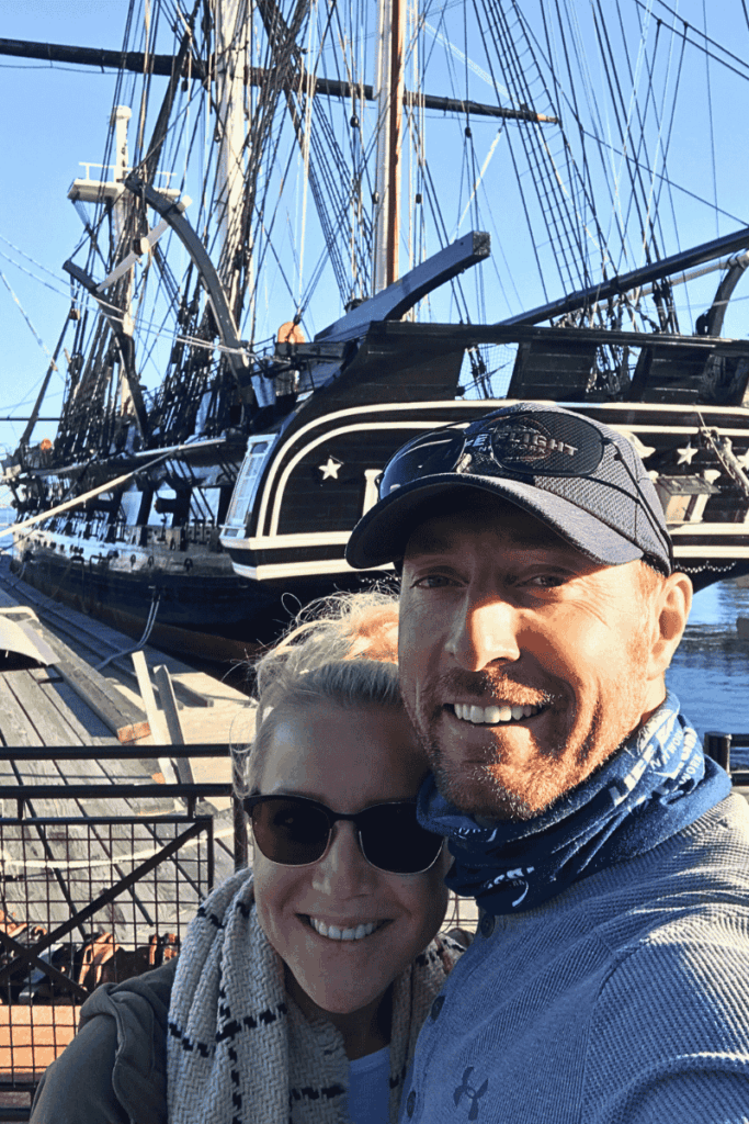 Kate and her husband smiling in front of the USS Constitution, also known as “Old Ironsides,” docked in the Charlestown Navy Yard. 