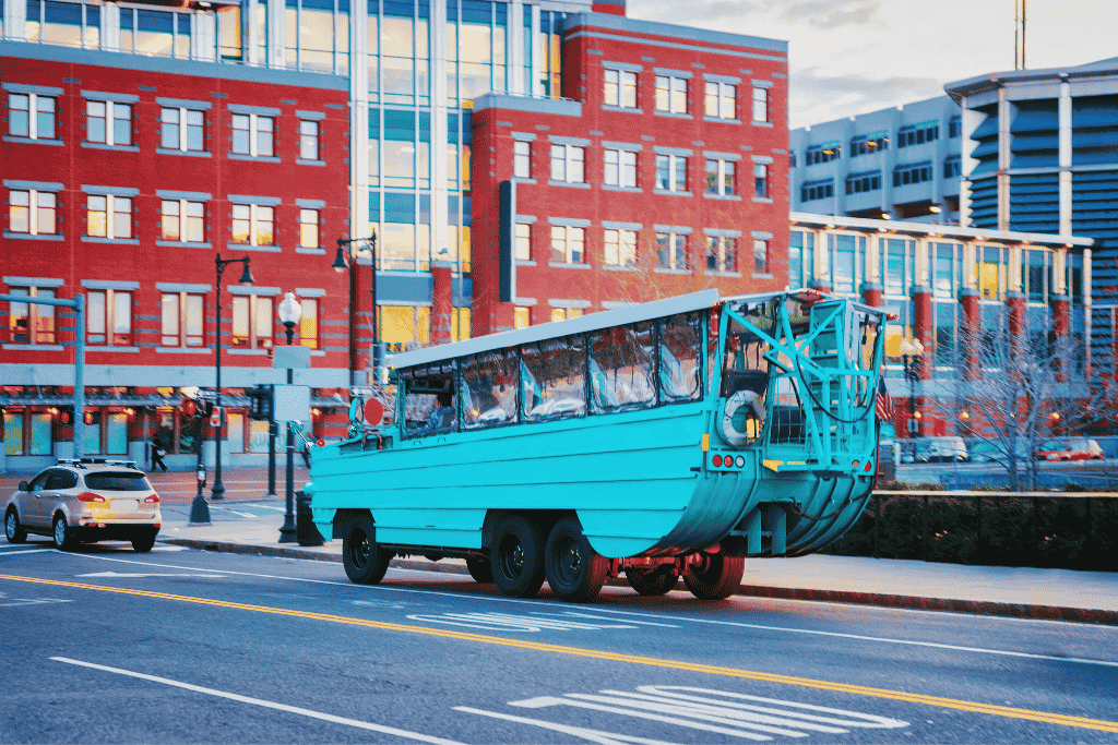 Bright blue Boston Duck Tour vehicle driving through the city streets with a red brick building in the background. A quirky and fun sightseeing experience during a weekend getaway in Boston.