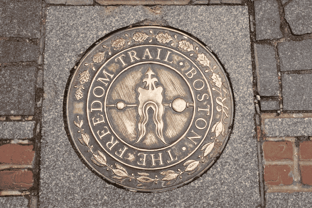 Close-up of the Freedom Trail medallion embedded in a cobblestone path in Boston, featuring an arrow and decorative leaves around the edge. A classic sight during a historic weekend getaway in Boston.







