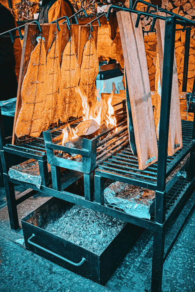 Slices of salmon fillets are wood-planked and flame-grilled over an open fire at a rustic food stall in the Brussels Christmas Market.

