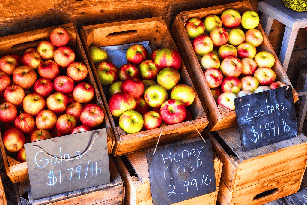 Wooden crates filled with Gala, Honeycrisp, and Zestar apples sit on display with handwritten price signs at a farm stand.