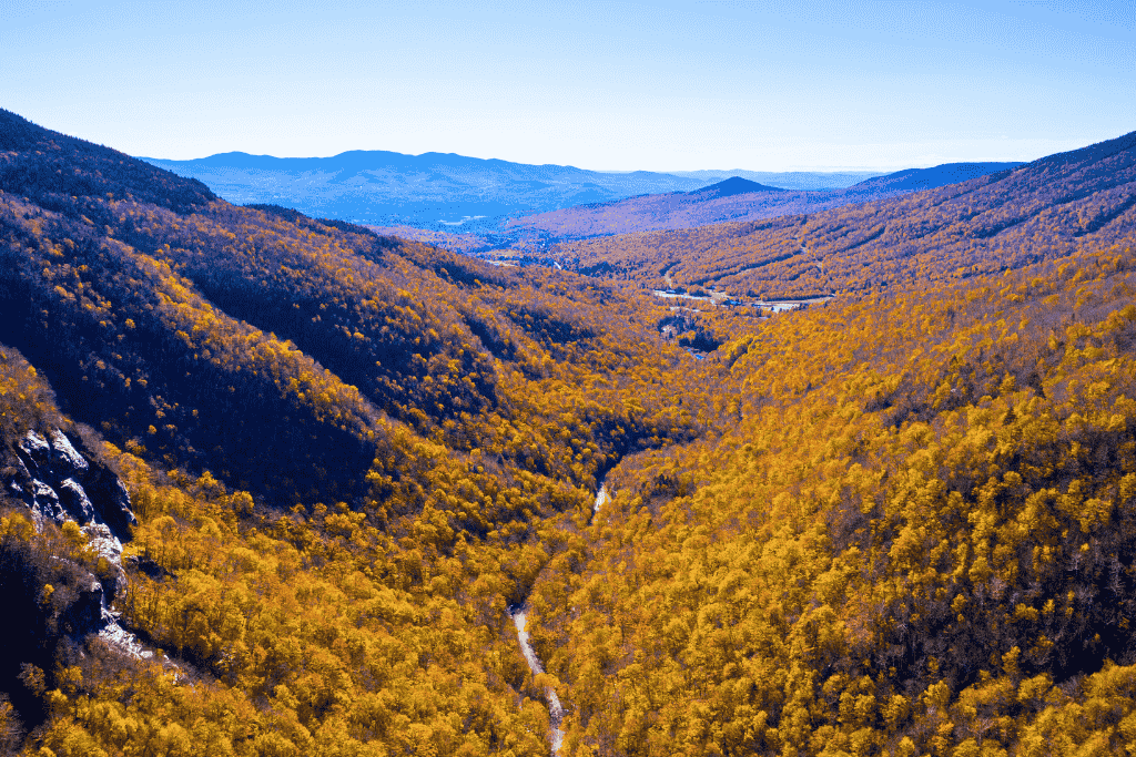 A winding road cuts through the golden fall foliage of Smugglers’ Notch State Park, nestled between steep mountain slopes in Vermont.
