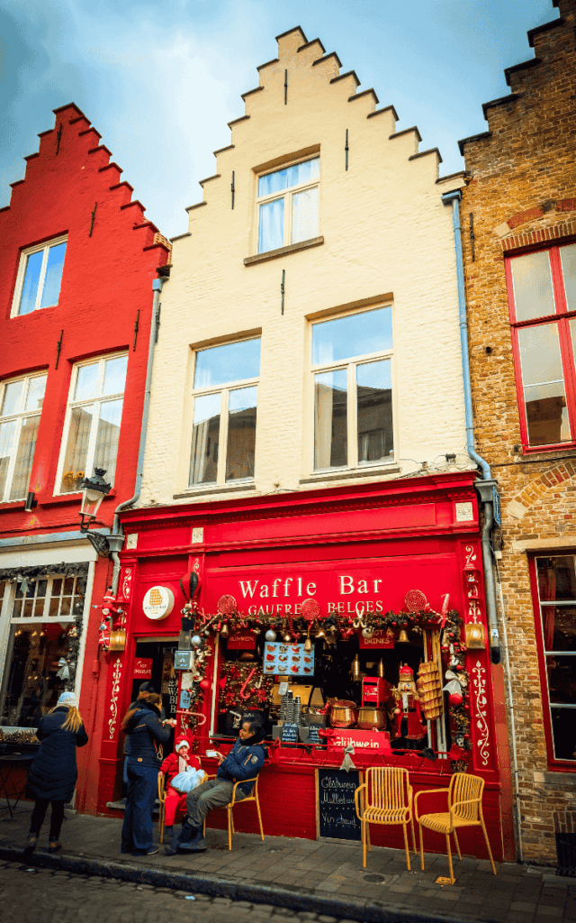 A bright red waffle bar in Bruges is decorated for Christmas with garlands, ornaments, and festive signage.