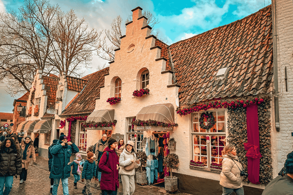 Shoppers stroll past whitewashed gabled buildings decorated with wreaths and garlands in Bruges.
