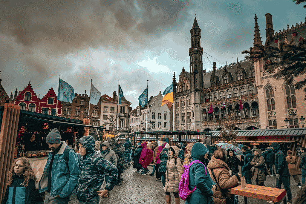 Crowds explore the Bruges Christmas Market surrounded by colorful gabled buildings and the ornate Gothic City Hall.