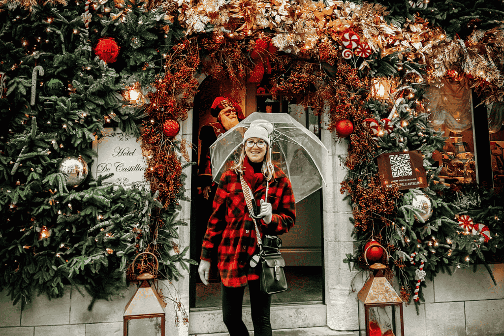 Kate stands under a clear umbrella in the doorway of Hotel De Castillion, framed by lavish gold and red Christmas decorations.