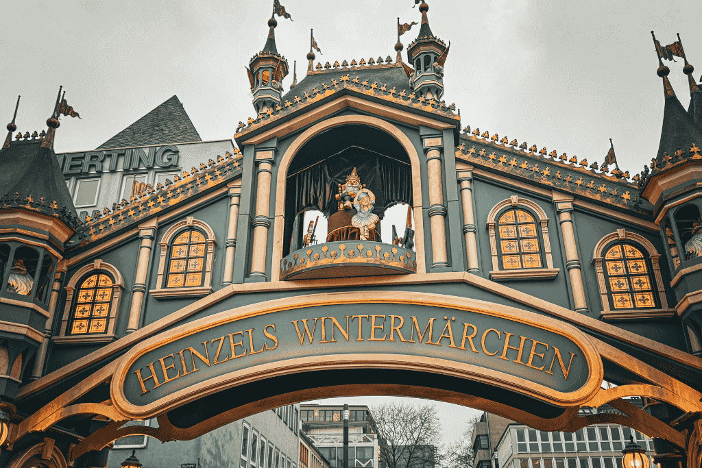 Close-up of the ornate Heinzel’s Wintermärchen entrance at the Cologne Christmas Market, featuring golden trim, arched windows, and a whimsical gnome figure on a balcony.
