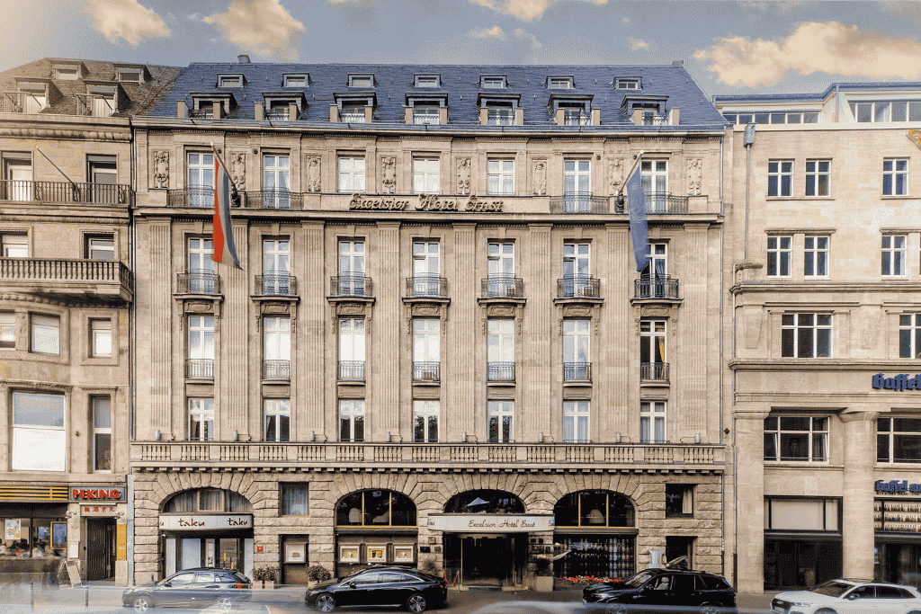 The grand stone facade of Excelsior Hotel Ernst in Cologne features tall windows, decorative columns, and national flags above its entrance.