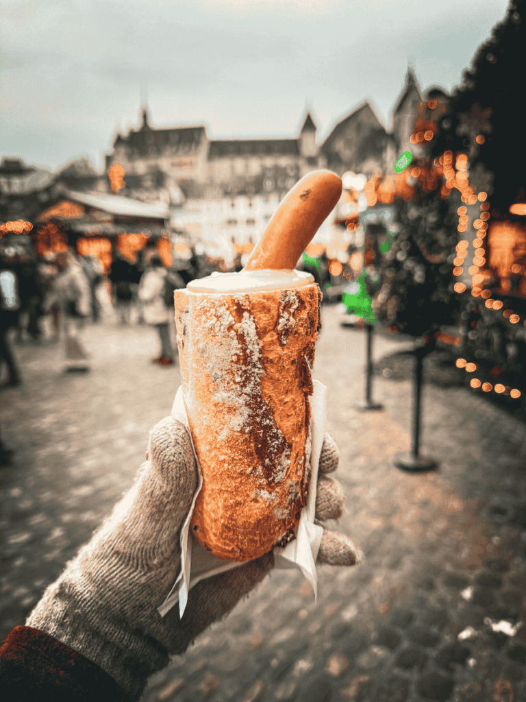 A sausage served in a hollowed bread roll is held up against the festive backdrop of the market.