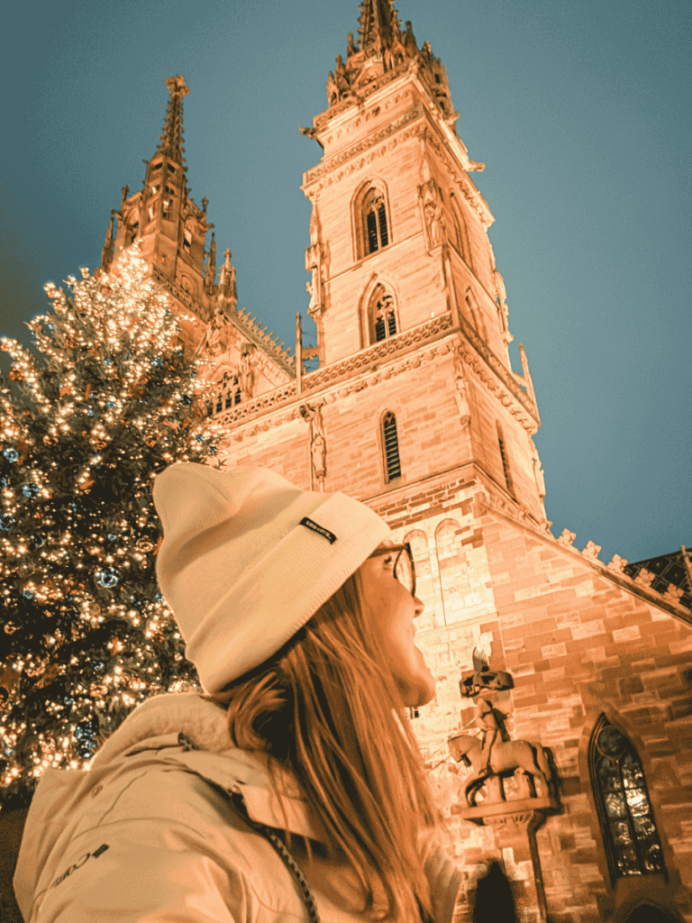 Kate looks up in awe at Basel Minster lit warmly beside a decorated Christmas tree.