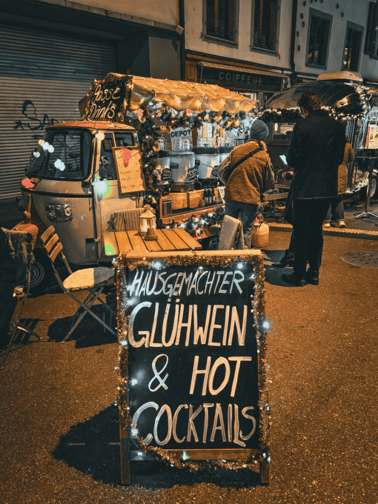 A decorated street stall sign advertises homemade Glühwein and hot cocktails.