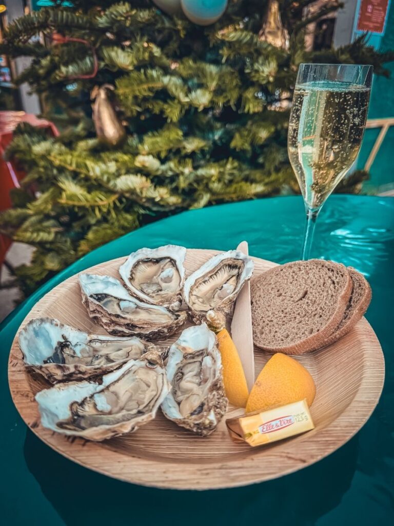 A festive plate of oysters with lemon, bread, and butter is served with a glass of sparkling wine by a Christmas tree.