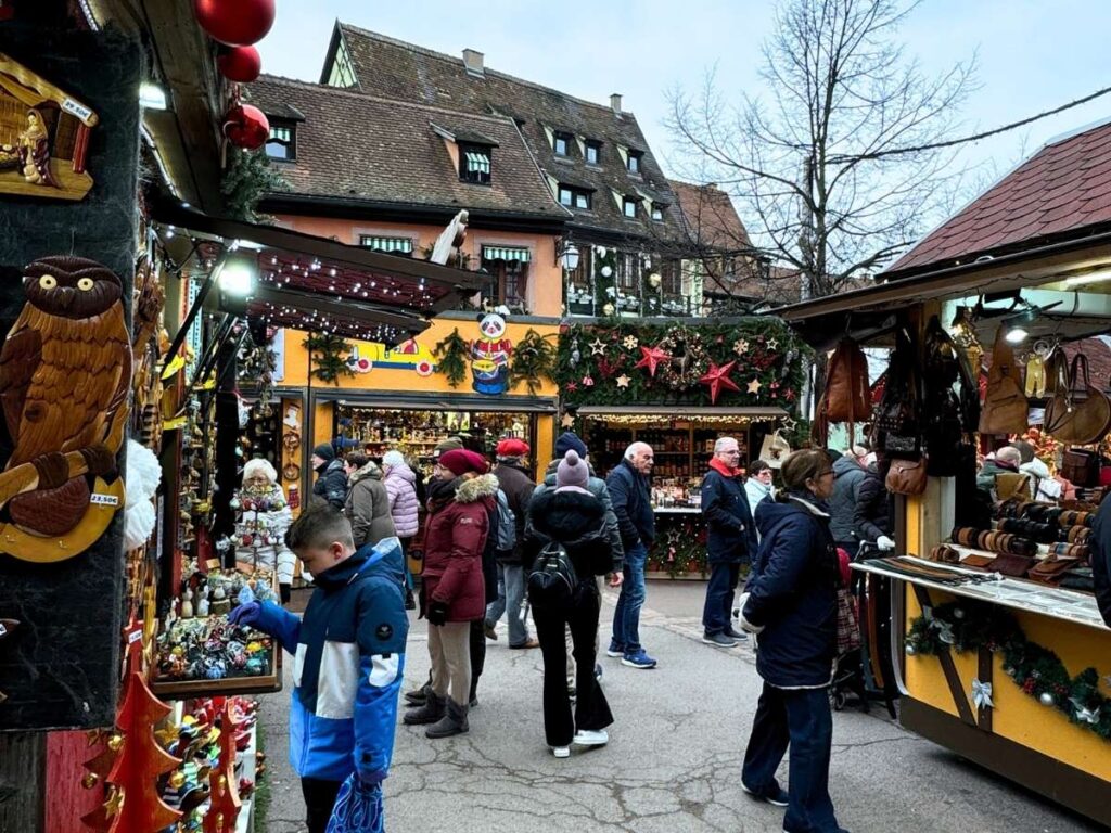 Shoppers browse festive stalls decorated with lights and ornaments at the Colmar Christmas market.