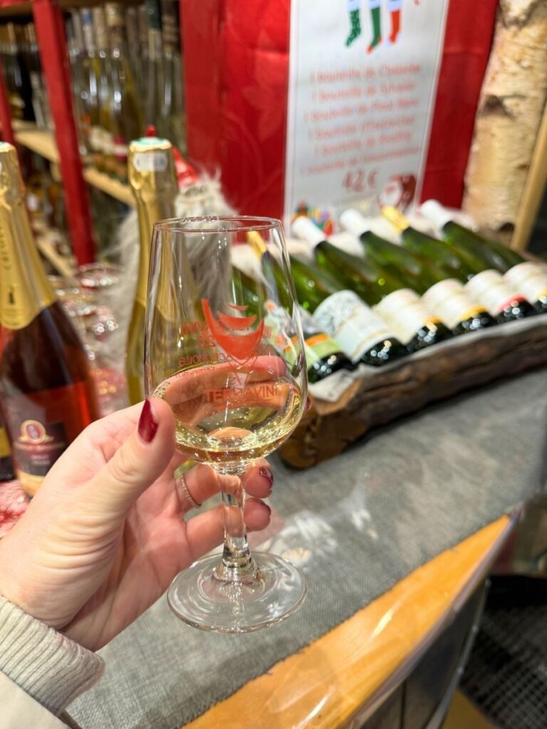 A glass of white wine is held up for tasting at a festive stall in Colmar.