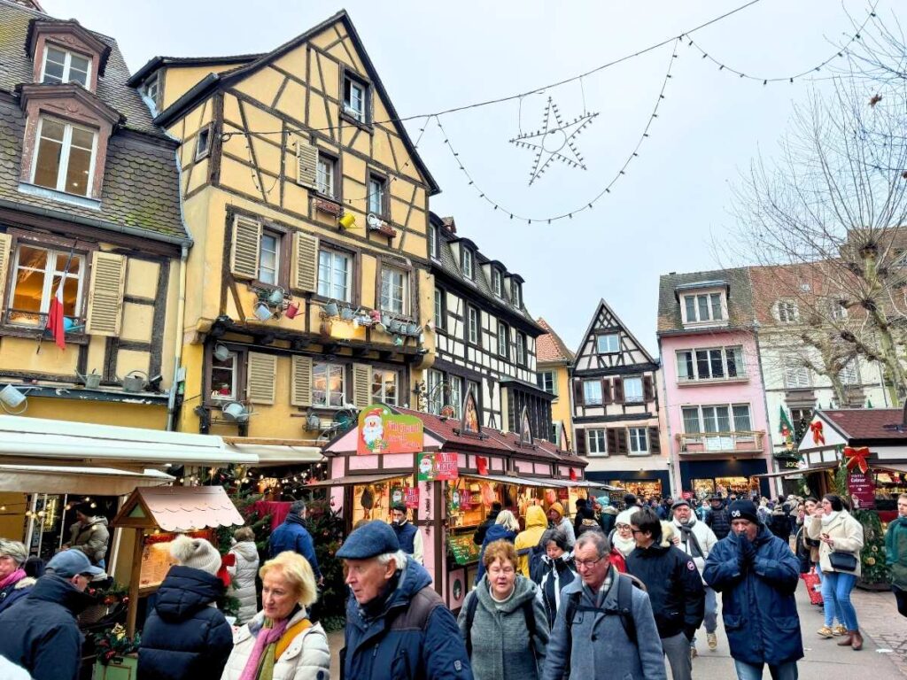 Crowds stroll past half-timbered houses and festive stalls at the Colmar Christmas market.