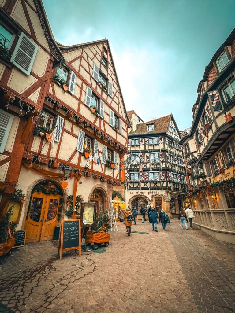 A charming cobblestone street in Colmar is lined with half-timbered houses decorated for Christmas.